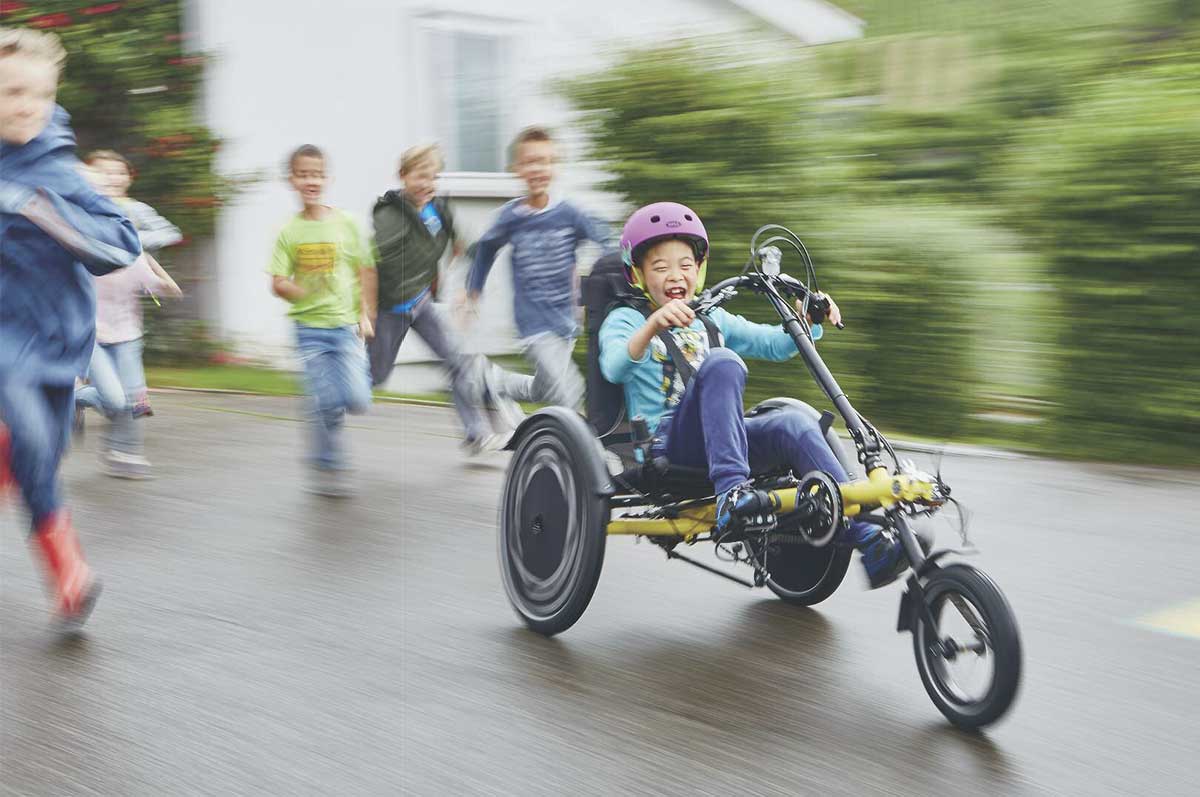 girl riding a hase trets adaptive recumbent trike with friends running alongside her
