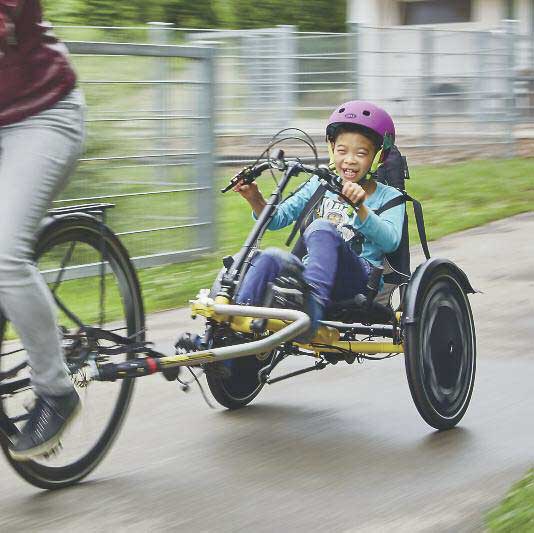 boy riding a hase trets adaptive recumbent trike as a trailer behind a parent on a bike